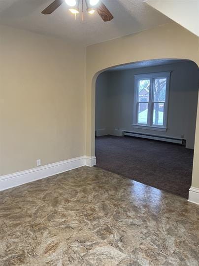 spare room featuring a baseboard heating unit, ceiling fan, arched walkways, and baseboards