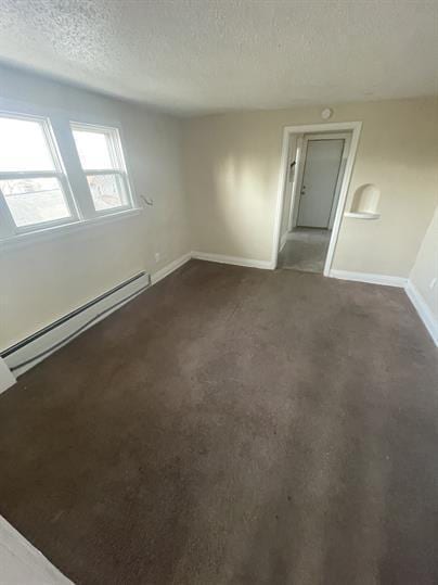 spare room featuring a baseboard heating unit, baseboards, dark colored carpet, and a textured ceiling
