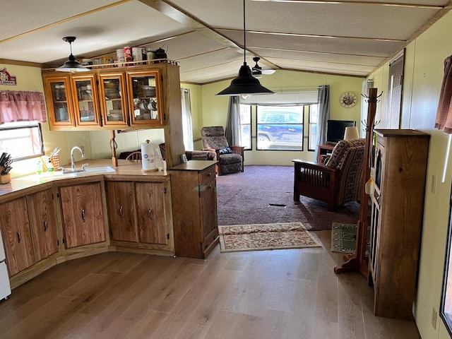 kitchen with brown cabinetry, a sink, wood finished floors, and vaulted ceiling