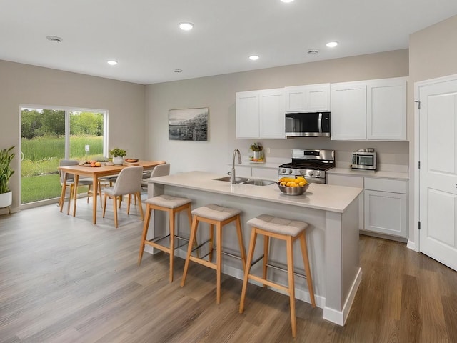 kitchen featuring appliances with stainless steel finishes, a sink, wood finished floors, a kitchen breakfast bar, and light countertops