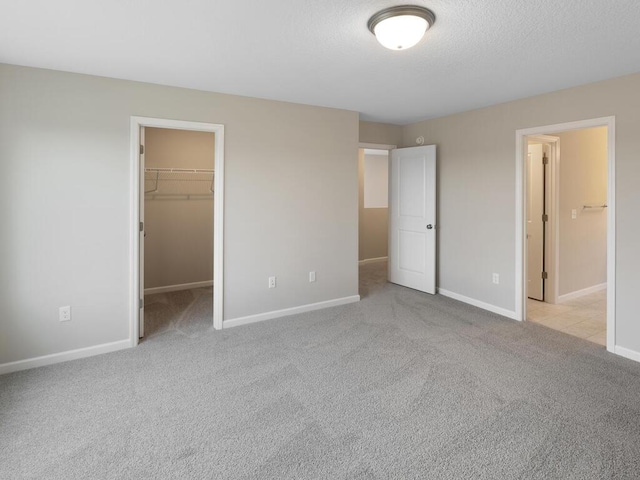 unfurnished bedroom featuring light carpet, a walk in closet, a textured ceiling, baseboards, and a closet