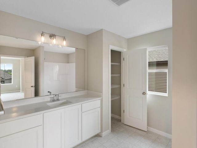 bathroom with vanity, baseboards, tile patterned flooring, a shower, and a walk in closet