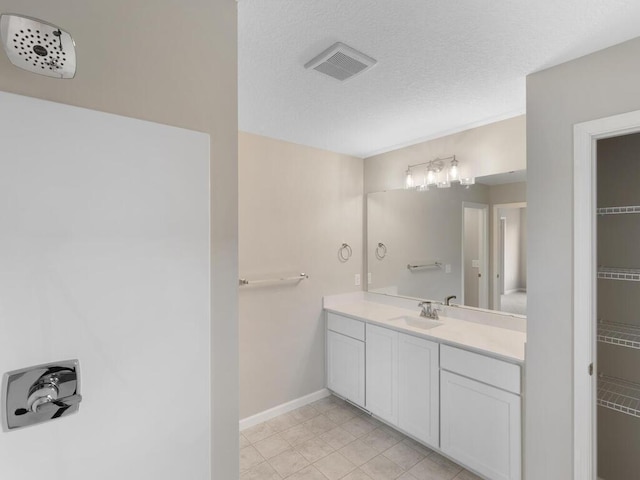 full bath featuring vanity, tile patterned flooring, baseboards, a textured ceiling, and a spacious closet