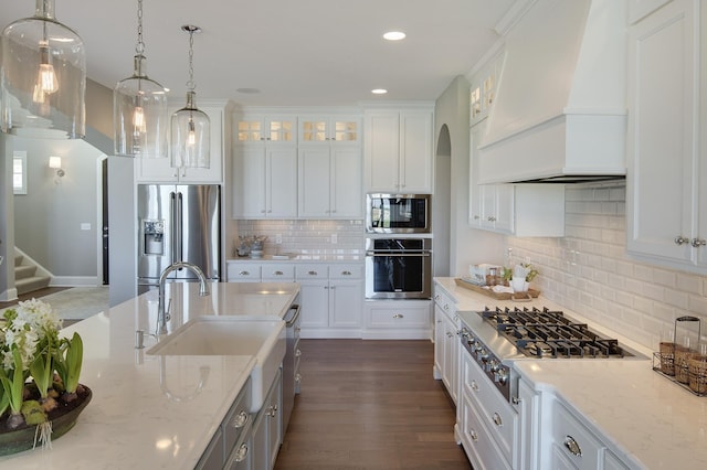 kitchen with arched walkways, white cabinetry, custom range hood, appliances with stainless steel finishes, and recessed lighting