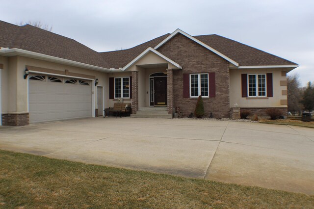 ranch-style house featuring roof with shingles, a garage, brick siding, concrete driveway, and stucco siding