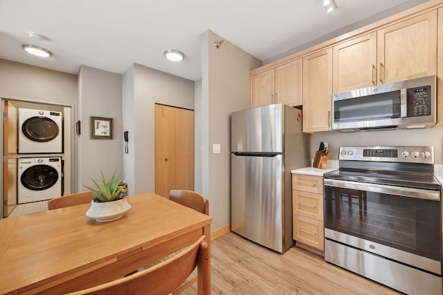 kitchen featuring stacked washer / drying machine, light brown cabinetry, appliances with stainless steel finishes, light countertops, and light wood finished floors