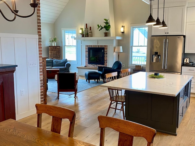 kitchen with white cabinetry, light wood-style floors, vaulted ceiling, a fireplace, and stainless steel fridge