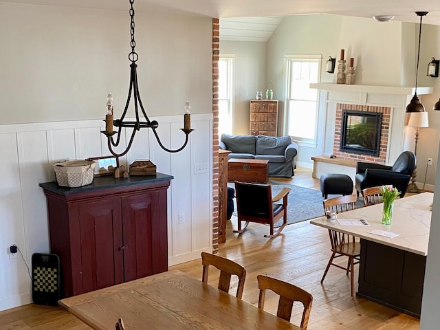 interior space featuring a wainscoted wall, a fireplace, light wood-style flooring, and vaulted ceiling