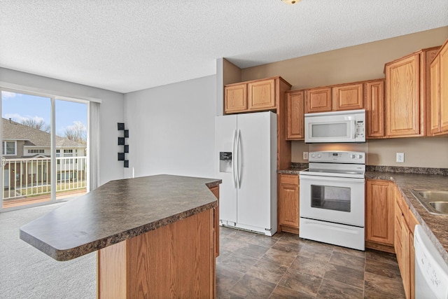 kitchen featuring dark countertops, a textured ceiling, a sink, white appliances, and a kitchen island