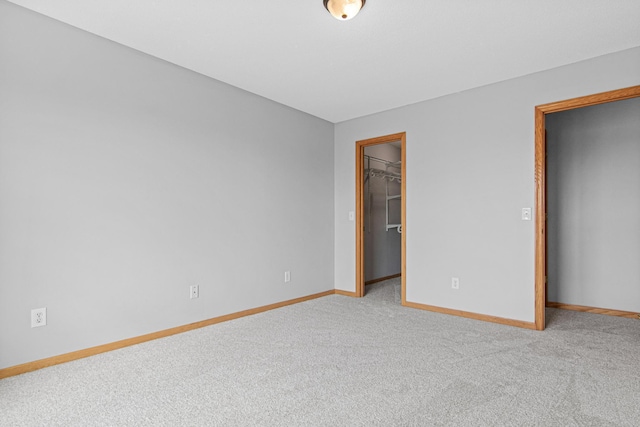unfurnished bedroom with carpet flooring, baseboards, a closet, and a walk in closet