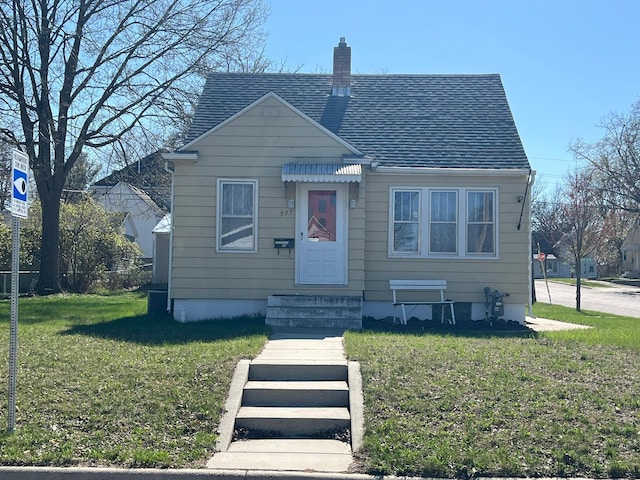 bungalow featuring entry steps, a chimney, a shingled roof, and a front yard