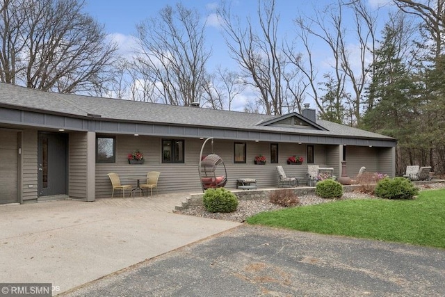 ranch-style house featuring covered porch, a front lawn, a chimney, and a shingled roof