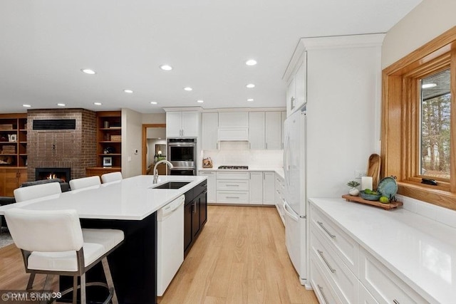 kitchen featuring white appliances, an island with sink, recessed lighting, and a sink
