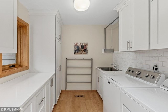 laundry area featuring light wood finished floors, a sink, washing machine and clothes dryer, cabinet space, and visible vents