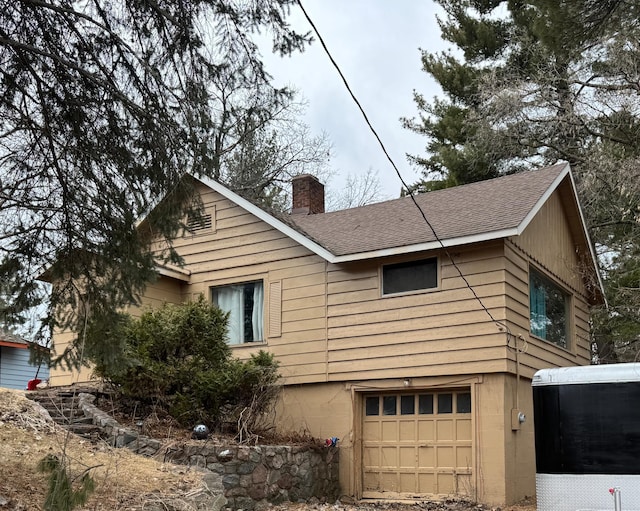view of home's exterior featuring a chimney, a shingled roof, and a garage