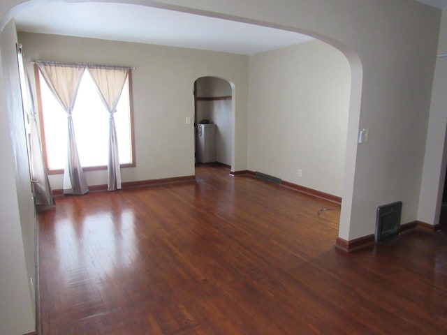 spare room featuring visible vents, baseboards, wood finished floors, and arched walkways