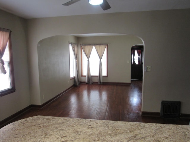 unfurnished room featuring wood finished floors, ceiling fan, arched walkways, baseboards, and visible vents