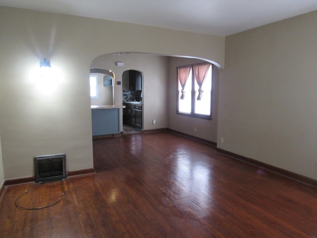 empty room featuring arched walkways, baseboards, visible vents, and dark wood-style floors