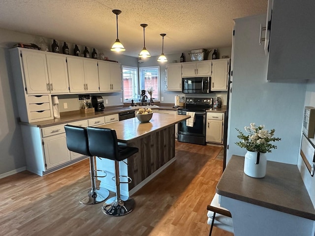 9808 Jenny Ln, Saint Wendel Twp, MN 56374 - kitchen with black appliances, a sink, a textured ceiling, wood finished floors, and a kitchen island
