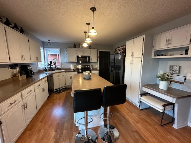9808 Jenny Ln, Saint Wendel Twp, MN 56374 - kitchen featuring black appliances, a textured ceiling, white cabinetry, a kitchen island, and wood finished floors