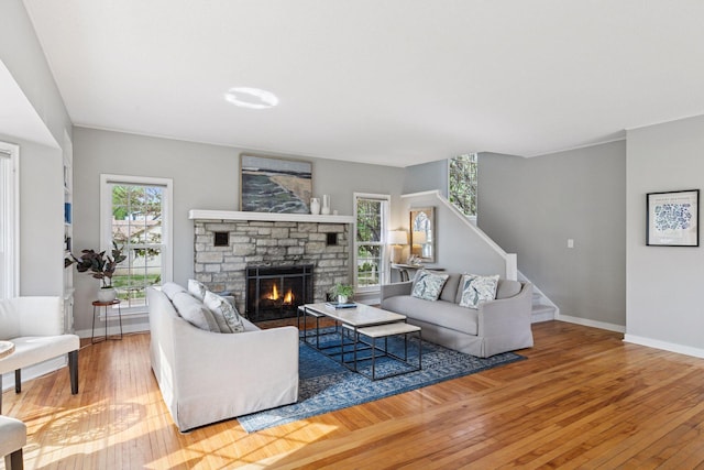 living room featuring wood-type flooring, a stone fireplace, baseboards, and stairs
