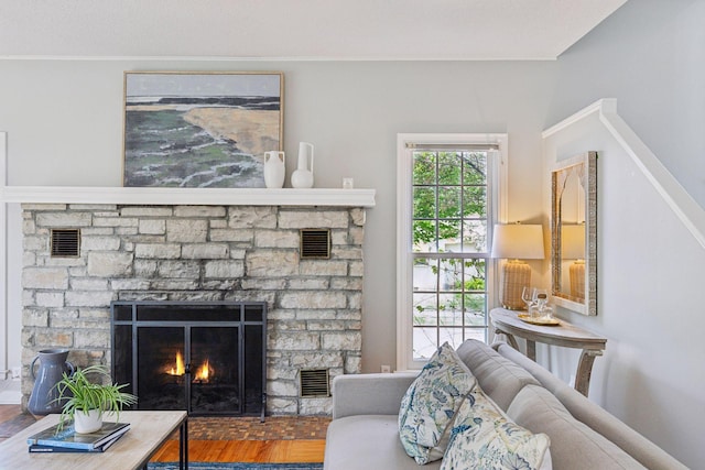 living area with a stone fireplace, wood finished floors, and crown molding