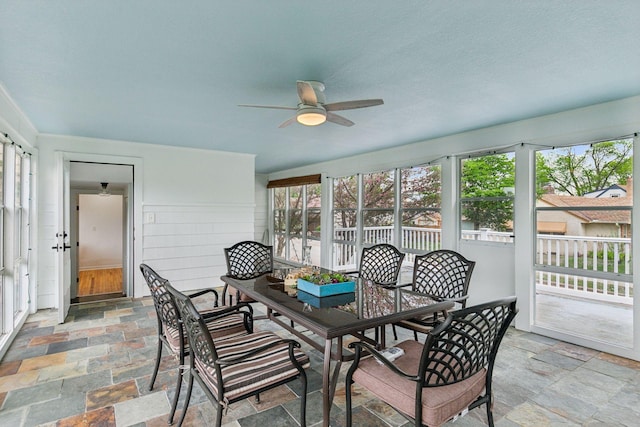 sunroom / solarium with stone tile flooring, ceiling fan, and outdoor dining space