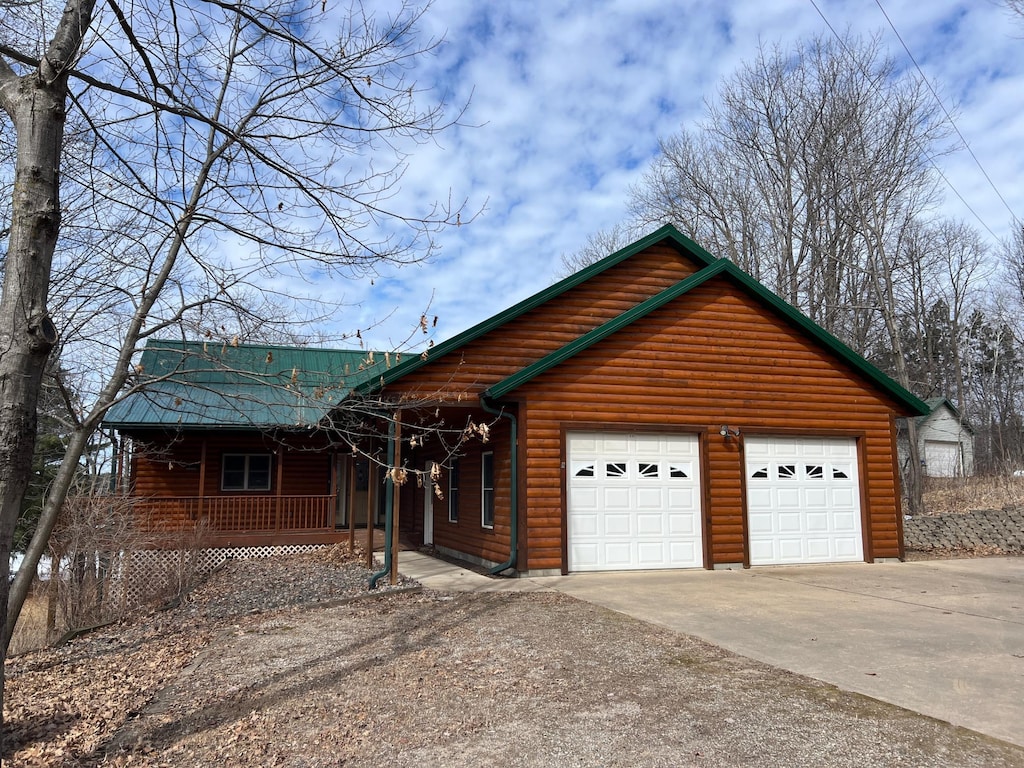 chalet / cabin featuring an attached garage, log veneer siding, a porch, concrete driveway, and metal roof
