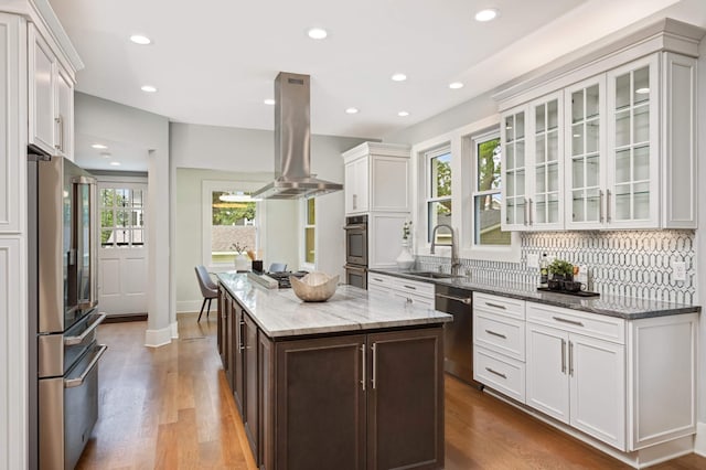 1647 26th St, Minneapolis, MN 55405 - kitchen featuring stainless steel appliances, island range hood, a sink, white cabinets, and glass insert cabinets