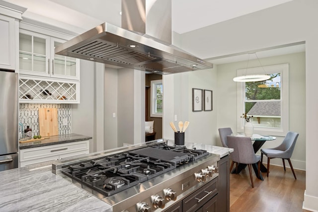 1647 26th St, Minneapolis, MN 55405 - kitchen featuring wall chimney range hood, stainless steel appliances, light stone countertops, wood finished floors, and decorative backsplash