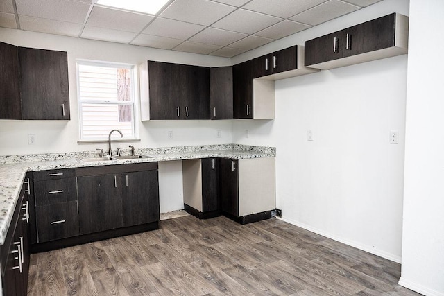 kitchen with a sink, a drop ceiling, baseboards, wood finished floors, and light stone countertops