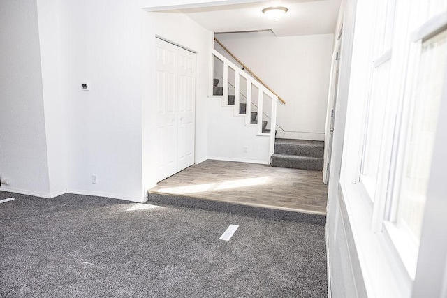 entryway with baseboards, dark colored carpet, and stairs