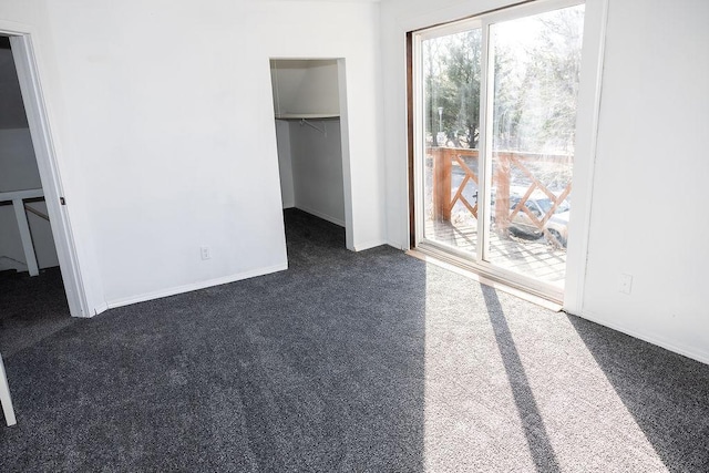 unfurnished bedroom with dark colored carpet, access to exterior, baseboards, a closet, and a walk in closet