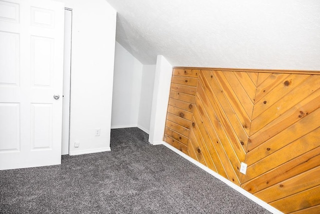 bonus room with baseboards and dark carpet
