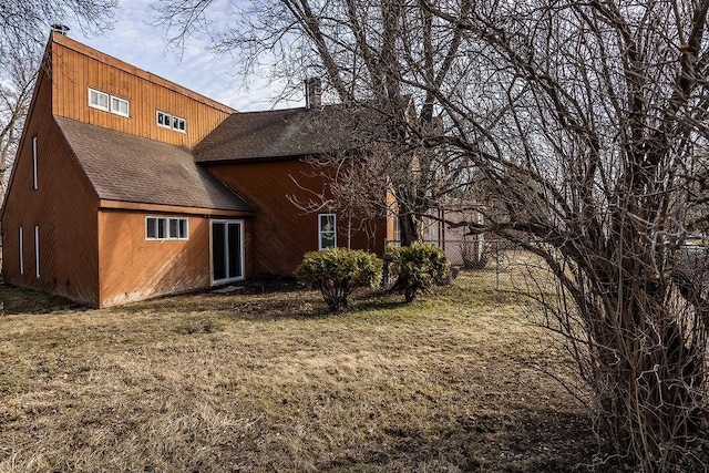 back of house featuring a yard, roof with shingles, a chimney, and fence