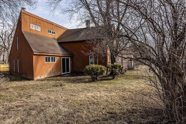 back of house with fence, a shingled roof, a chimney, and a yard
