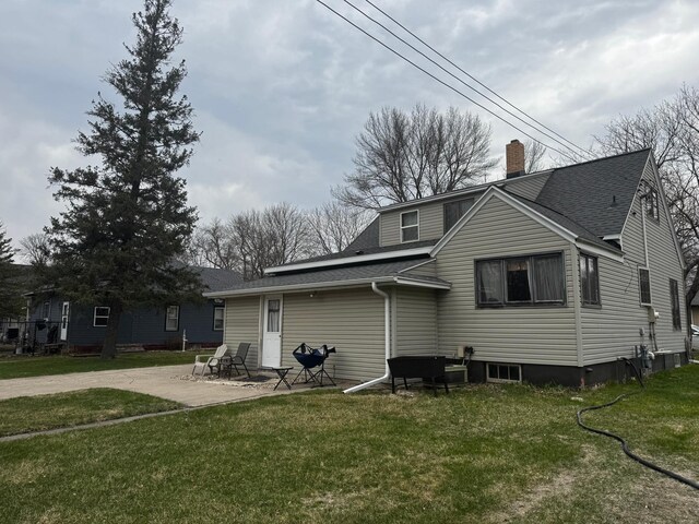 327 2nd St SW, Clara City, MN 56222 - rear view of house featuring roof with shingles, a chimney, a yard, and a patio