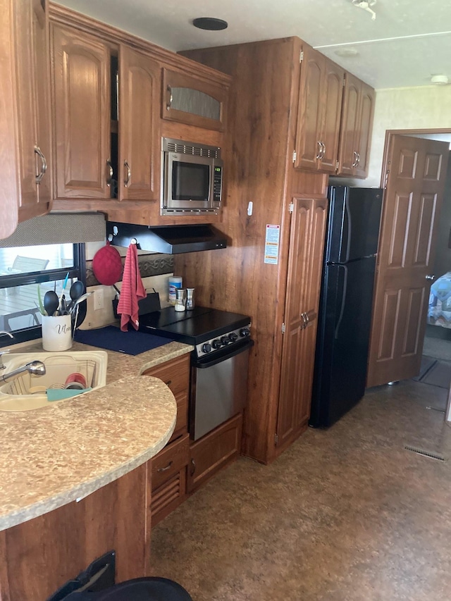kitchen with a sink, stainless steel microwave, freestanding refrigerator, electric range oven, and brown cabinetry