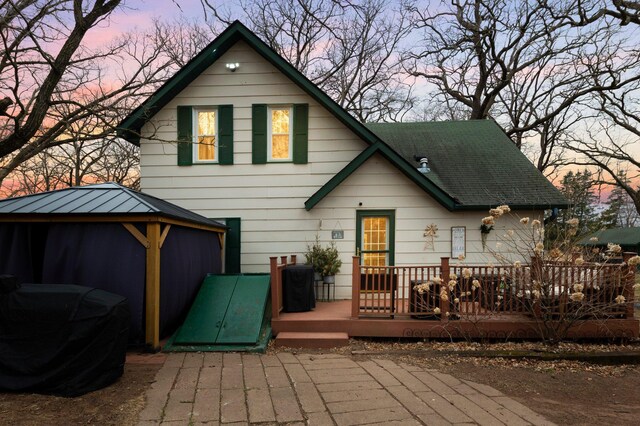 back of house at dusk with a shingled roof, a gazebo, and a deck