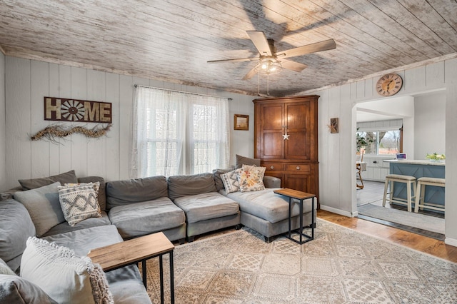 living area with arched walkways, light wood-type flooring, ceiling fan, wood ceiling, and wooden walls