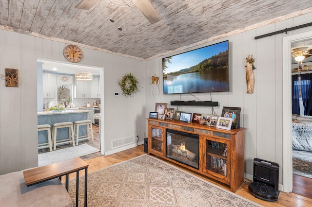 living room with light wood-type flooring, visible vents, a ceiling fan, crown molding, and wood ceiling