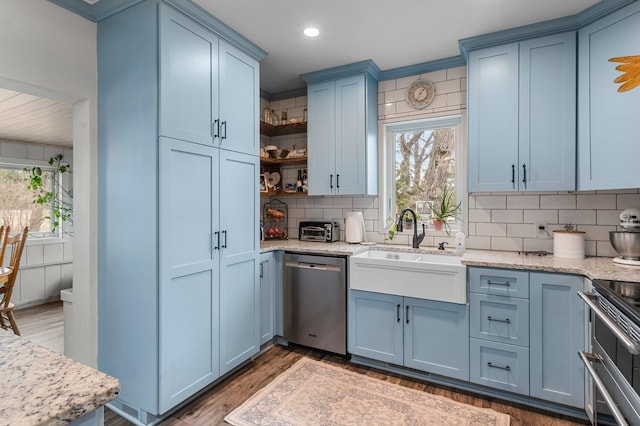 kitchen featuring blue cabinets, a sink, tasteful backsplash, light wood-style floors, and appliances with stainless steel finishes