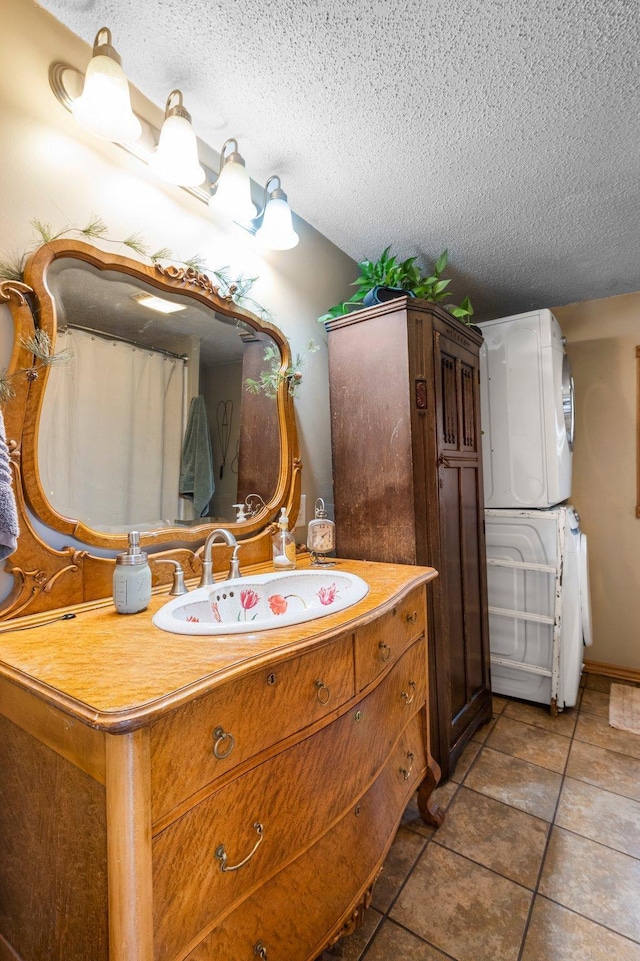 bathroom featuring a textured ceiling, stacked washer and dryer, tile patterned flooring, and vanity