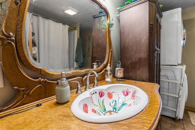 bathroom with a textured ceiling, stacked washer and dryer, baseboards, tile patterned flooring, and a shower with shower curtain
