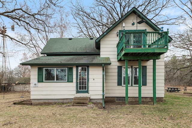 back of house featuring entry steps, roof with shingles, a balcony, and a lawn