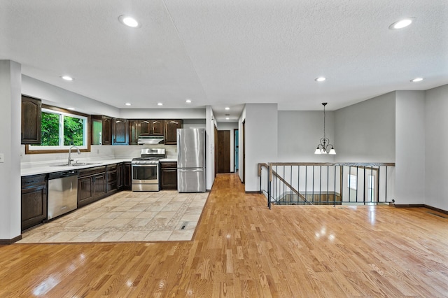 11560 Red Fox Dr, Maple Grove, MN 55369 - kitchen with stainless steel appliances, under cabinet range hood, a sink, light wood-type flooring, and dark brown cabinetry