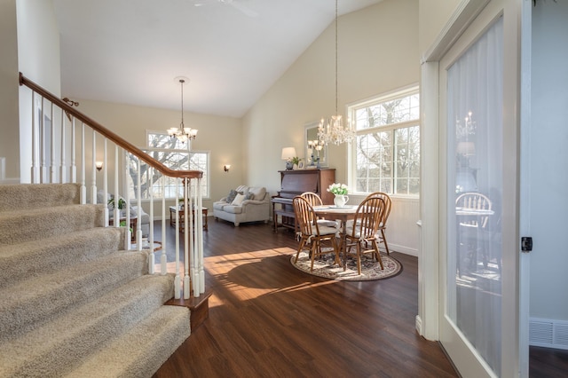 dining room with visible vents, dark wood finished floors, high vaulted ceiling, an inviting chandelier, and stairs
