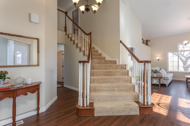 stairway featuring a towering ceiling, baseboards, wood finished floors, and a notable chandelier