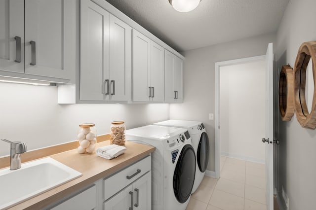clothes washing area with a sink, a textured ceiling, cabinet space, baseboards, and independent washer and dryer