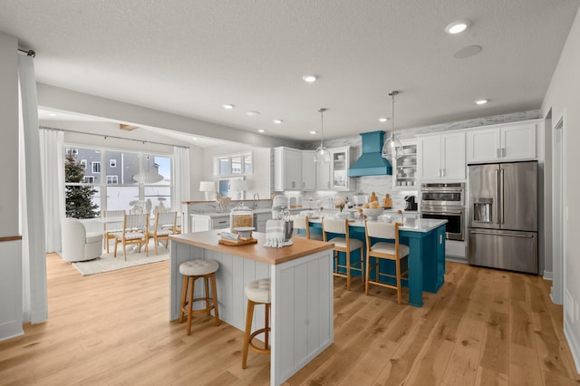 kitchen featuring a breakfast bar, stainless steel appliances, light wood-style flooring, custom range hood, and a kitchen island